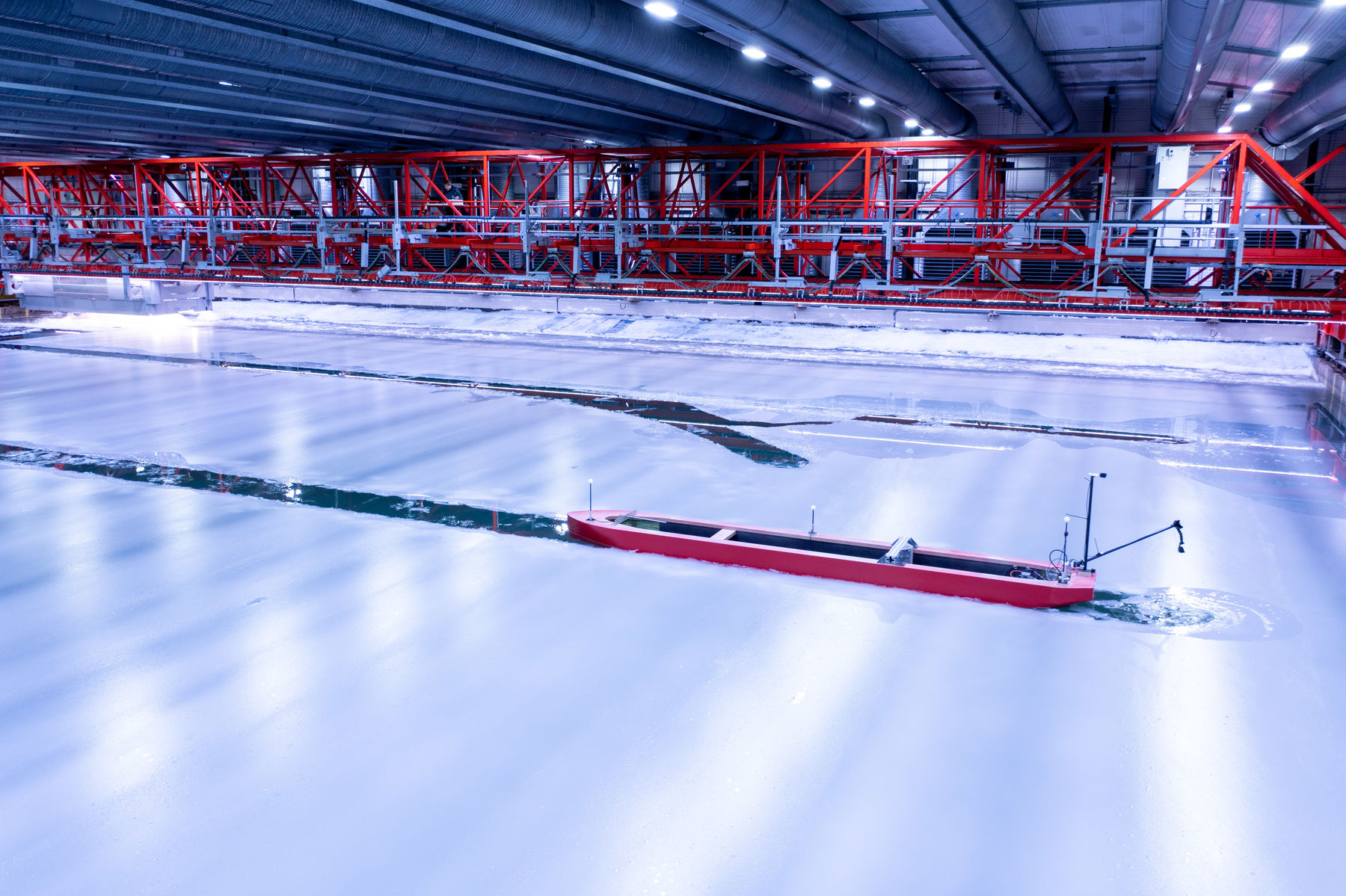 A red model ship breaks through the ice from left to right of the image middleground. In the background the red metal bridge is visible across the full width of the image. 