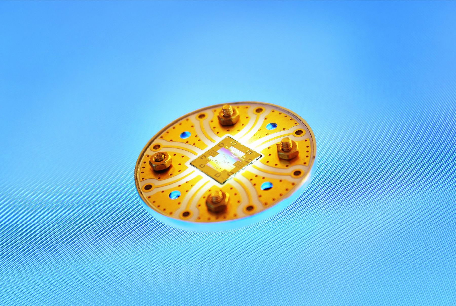 A circular gold quantum chip is illuminated on top of a blue background